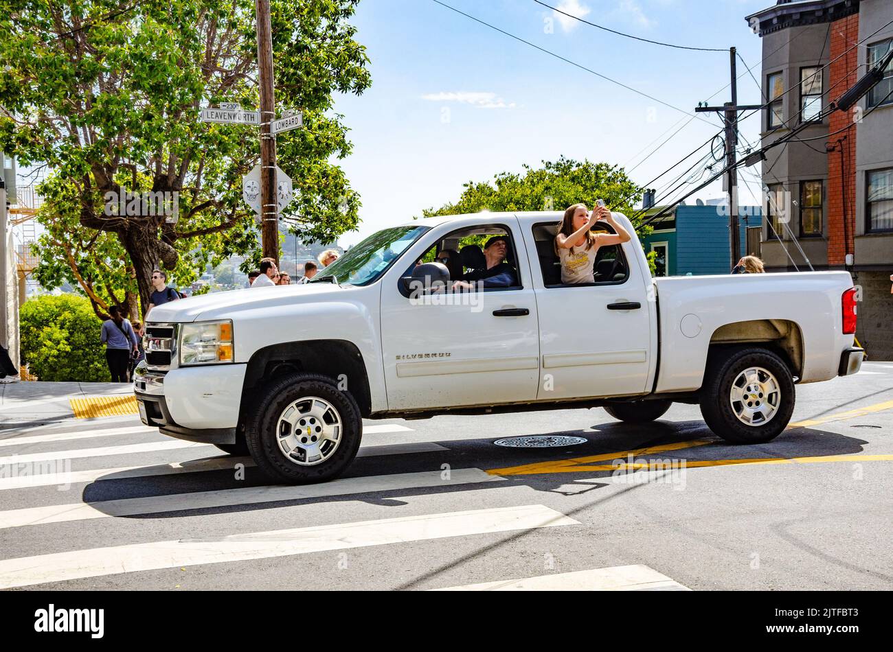 Una signora si appende fuori dalla finestra del passeggero di un camion bianco pick up per scattare una fotografia della famosa sezione di Lombard Street a San Francisco. Foto Stock