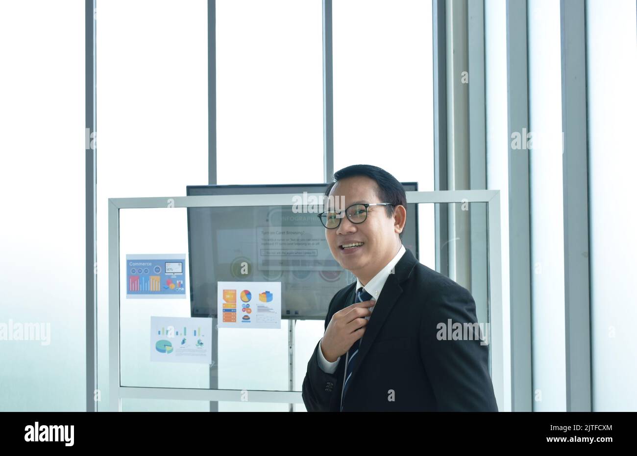 Uomo d'affari asiatico felice che tiene la cravatta prepararsi a presentare in ufficio stanza Foto Stock