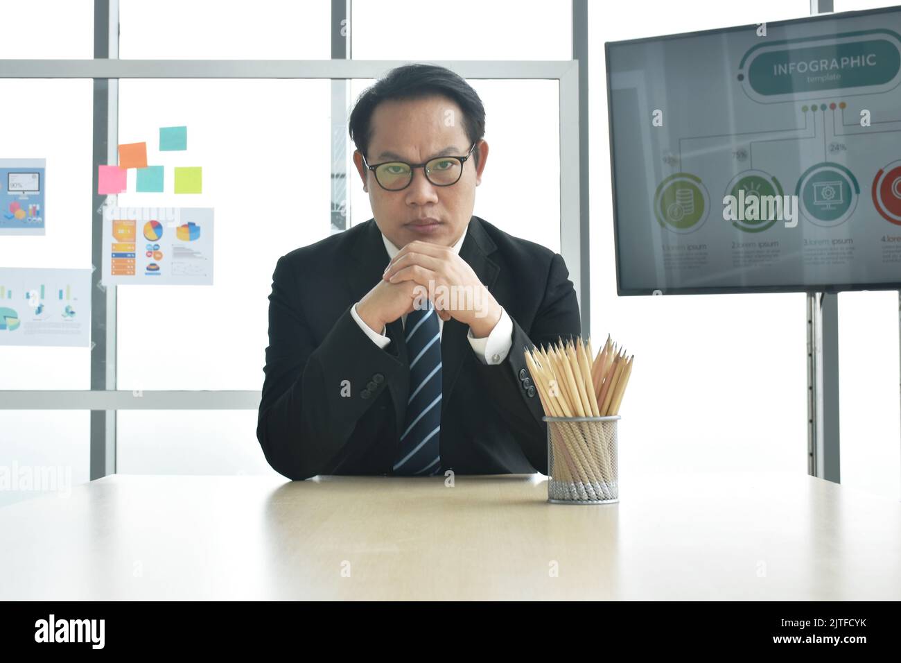 Un uomo d'affari asiatico serio, capo seduto alla scrivania nella sala riunioni dell'ufficio Foto Stock