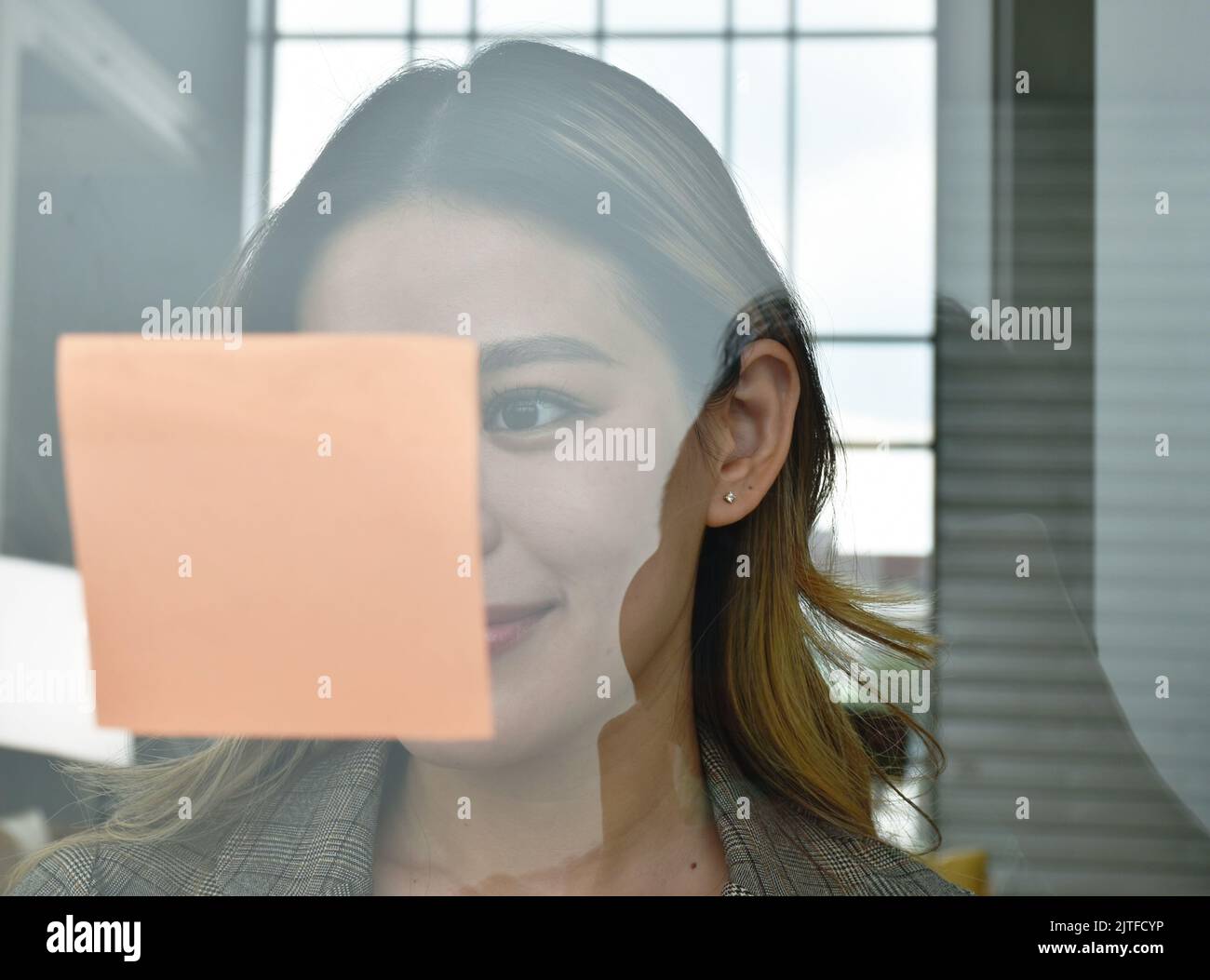 Felice donna asiatica busimess guardando la carta stick su vetro con momento di successo in ufficio Foto Stock