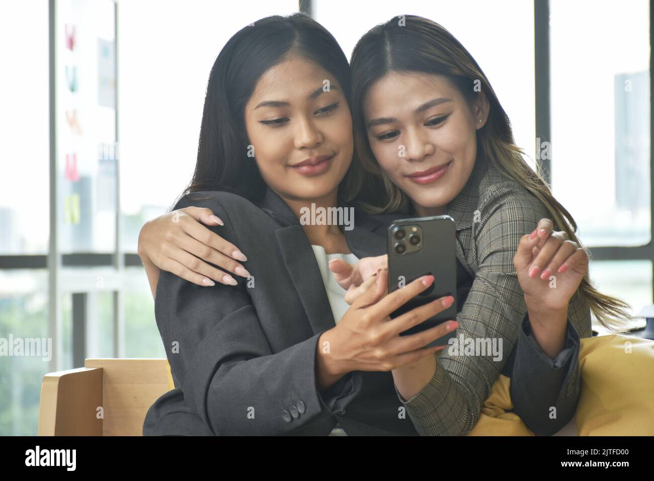 Felice due donne asiatiche busimess guardando il telefono cellulare per rilassarsi dopo il lavoro in ufficio Foto Stock