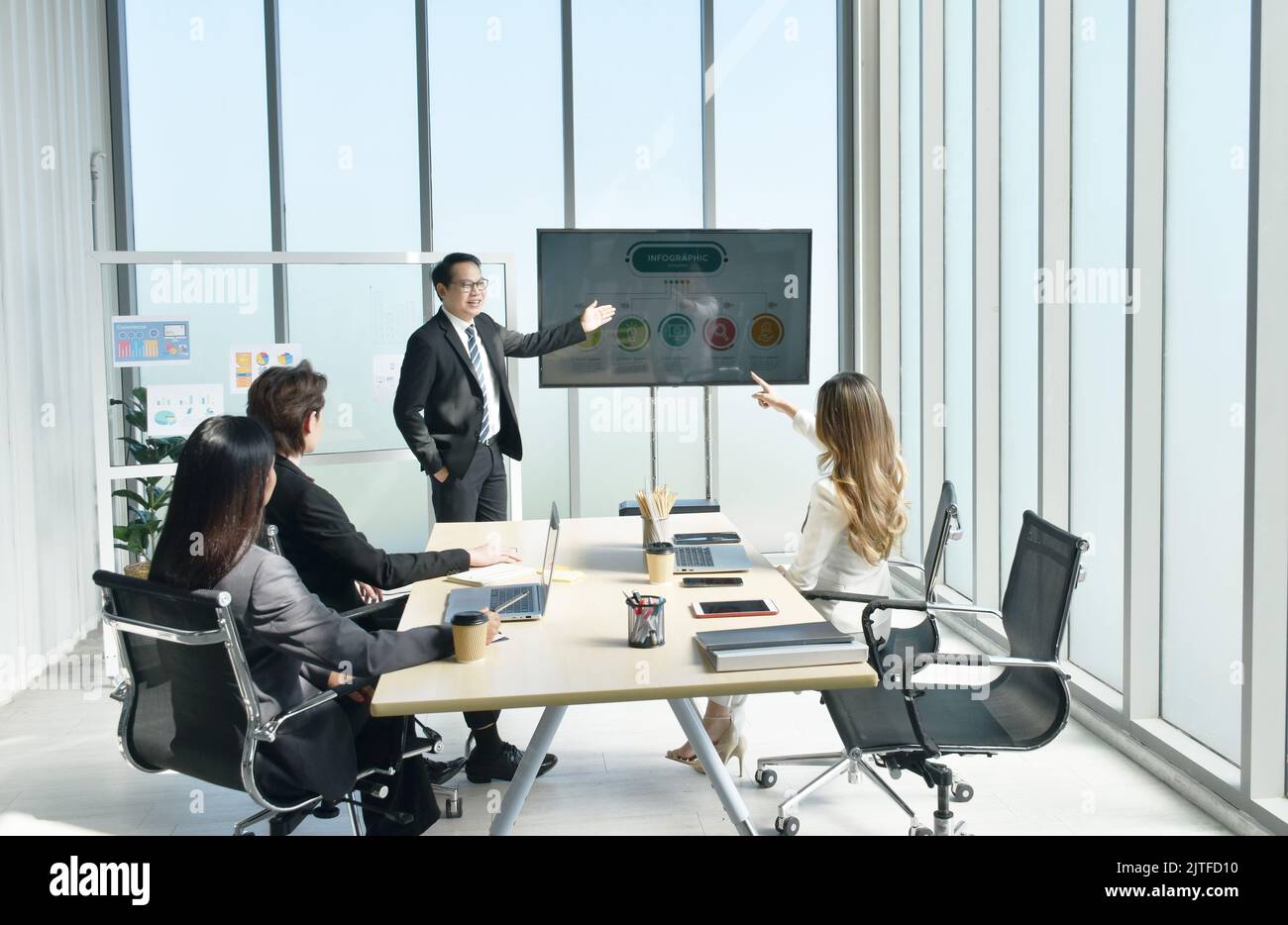 Uomo d'affari asiatico che presenta il lavoro sullo schermo della televisione con una donna che guarda il computer portatile nella sala riunioni dell'ufficio Foto Stock