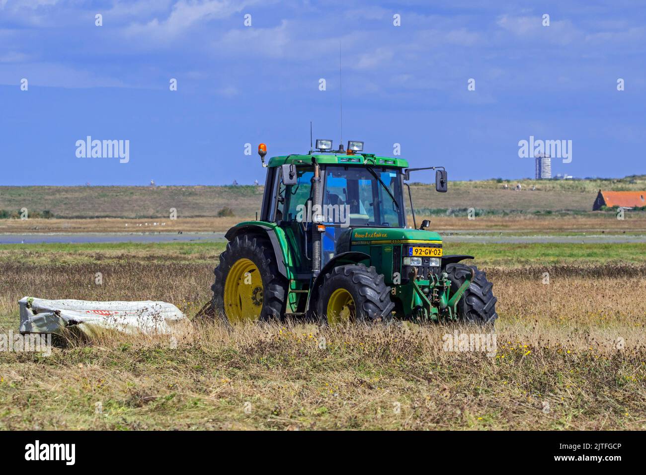 Trattore John Deere 6400 con falciatrice a disco che falcia erba in erba / prato in estate a Waterdunen, riserva naturale vicino a Breskens, Zeeland, Paesi Bassi Foto Stock