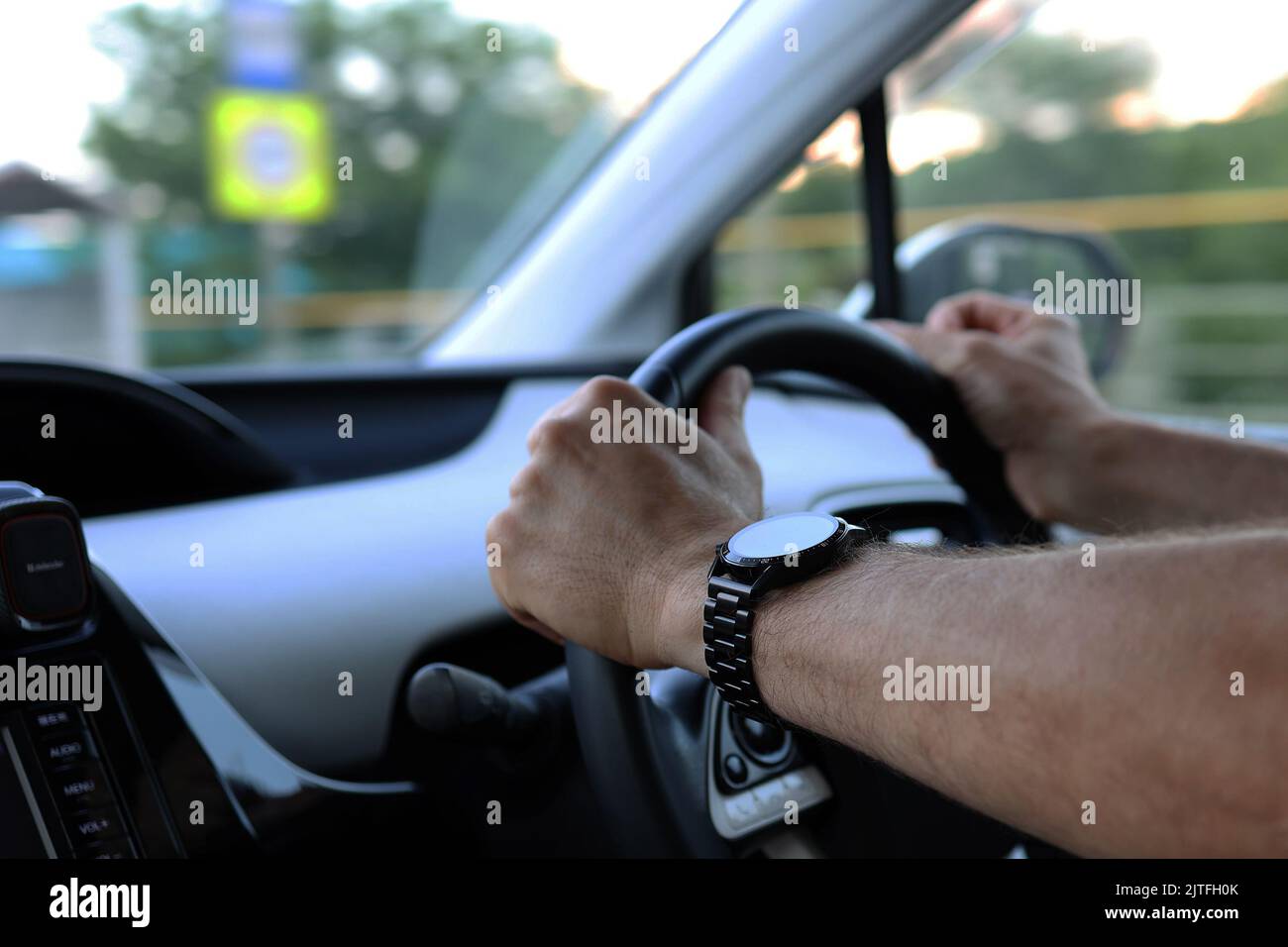 Belle mani maschili con un orologio intelligente che tiene il volante durante la guida di un'auto. Concetto di guida sicura Foto Stock