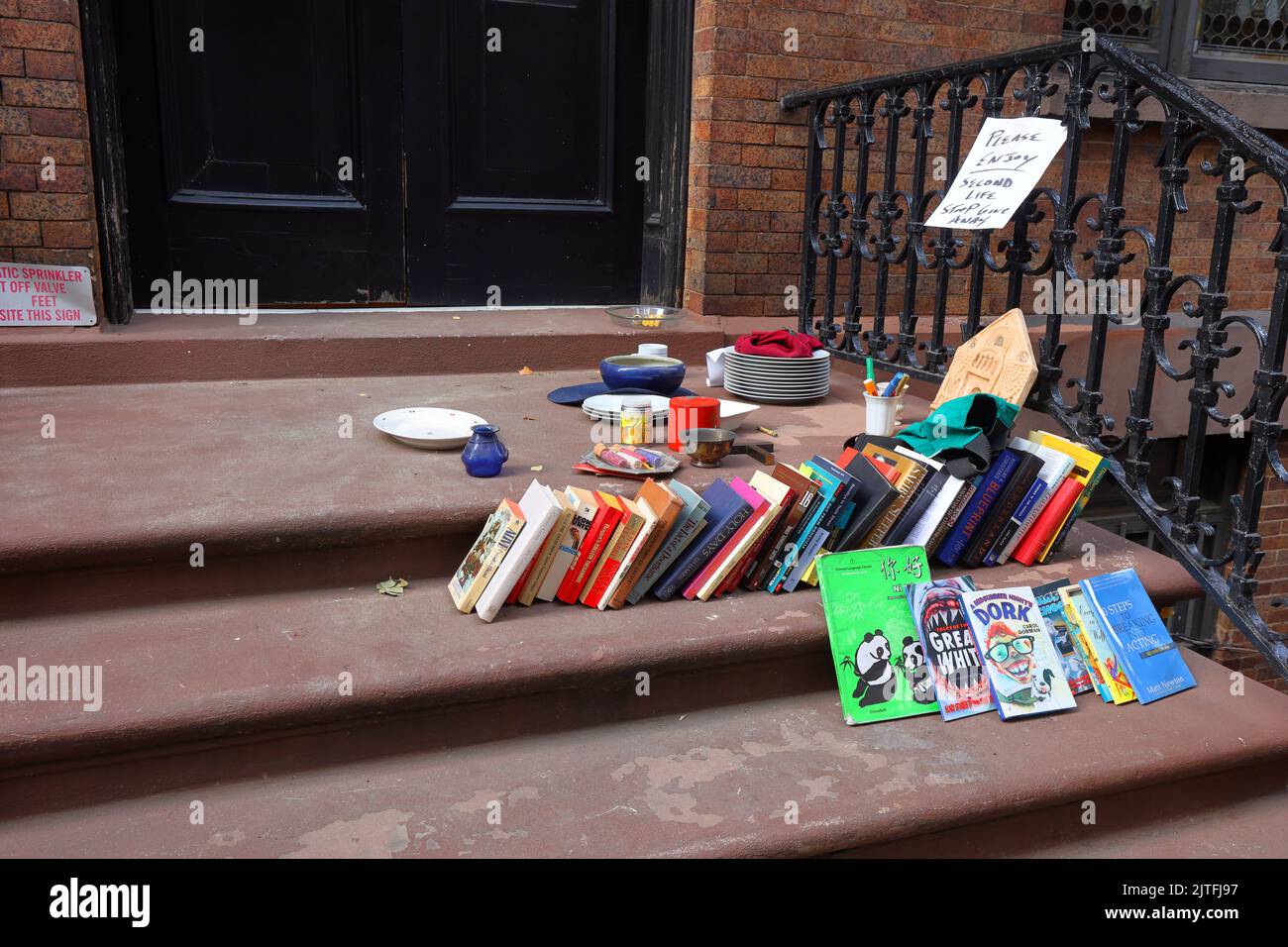 Libri, bric-a-brac, e altri oggetti liberi sulle scale di una casa cittadina in pietra marrone a New York per le persone che cercano gratuitamente stuff di stooping o frenare l'estrazione Foto Stock