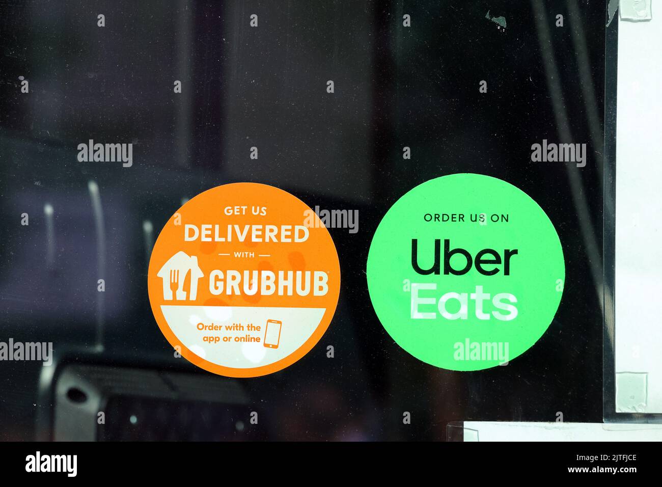 Grubhub e Uber mangiano gli adesivi dell'app dei servizi di consegna dei prodotti alimentari su una finestra che porta a un ristorante. Foto Stock