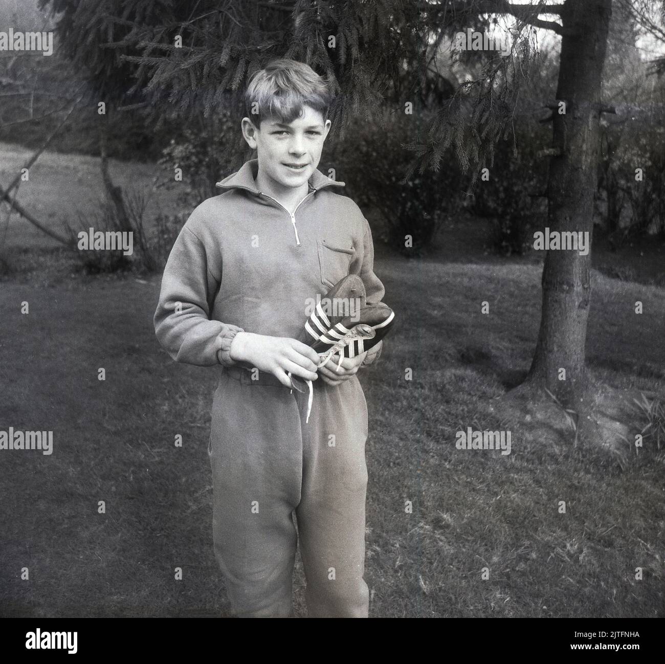 1962, storico, in piedi fuori, un adolescente in una tuta di cotone dell'epoca, tenendo scarpe da corsa pista, noto come a Spikes, Inghilterra, Regno Unito Foto Stock