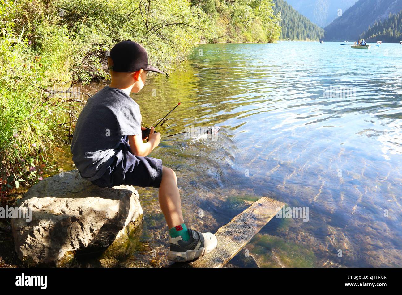 un ragazzino sul lago controlla una barca giocattolo Foto Stock