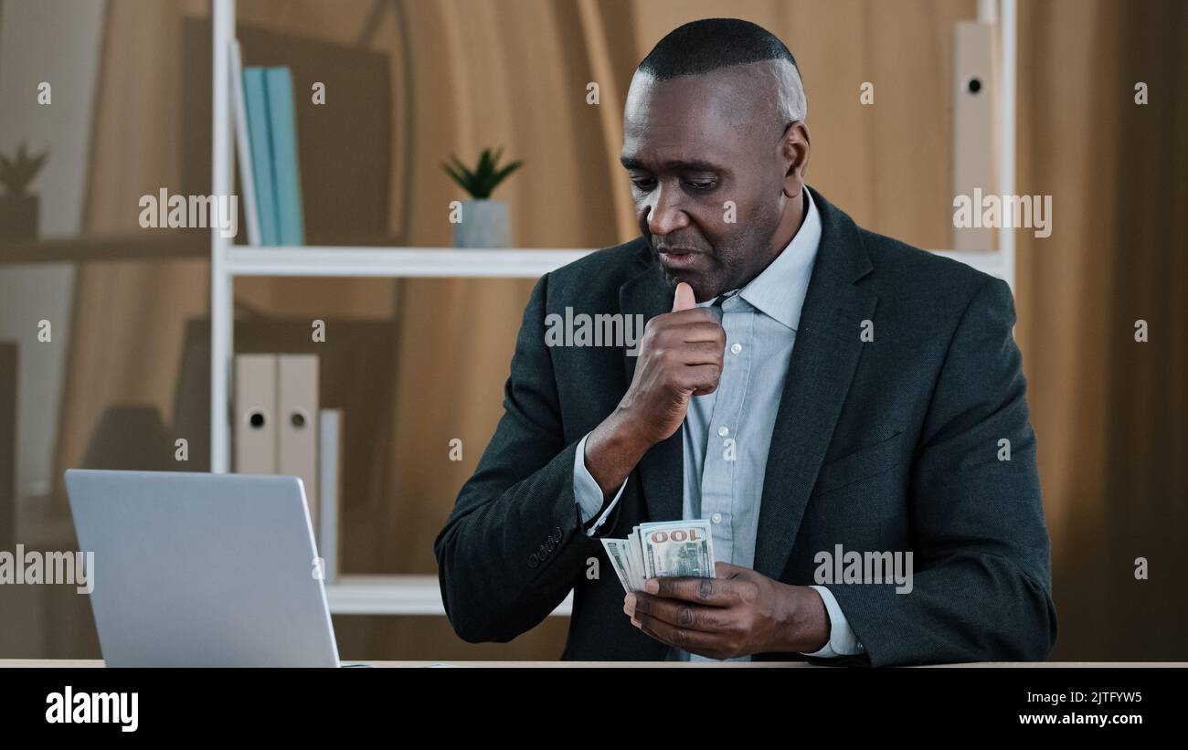 African vecchio maschio boss banchiere azienda CEO investitore senior maturo uomo d'affari conteggio di denaro in ufficio successo biracial uomo ricco in possesso di dollari Foto Stock