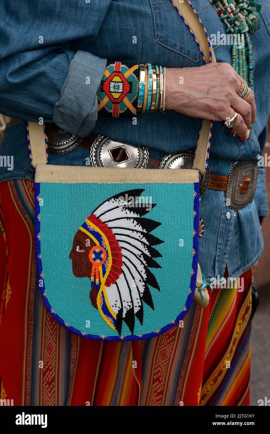 Una donna vestita con accessori dei nativi americani porta con sé una borsa con perline mentre visita il mercato indiano di Santa Fe a Santa Fe, New Mexico. Foto Stock