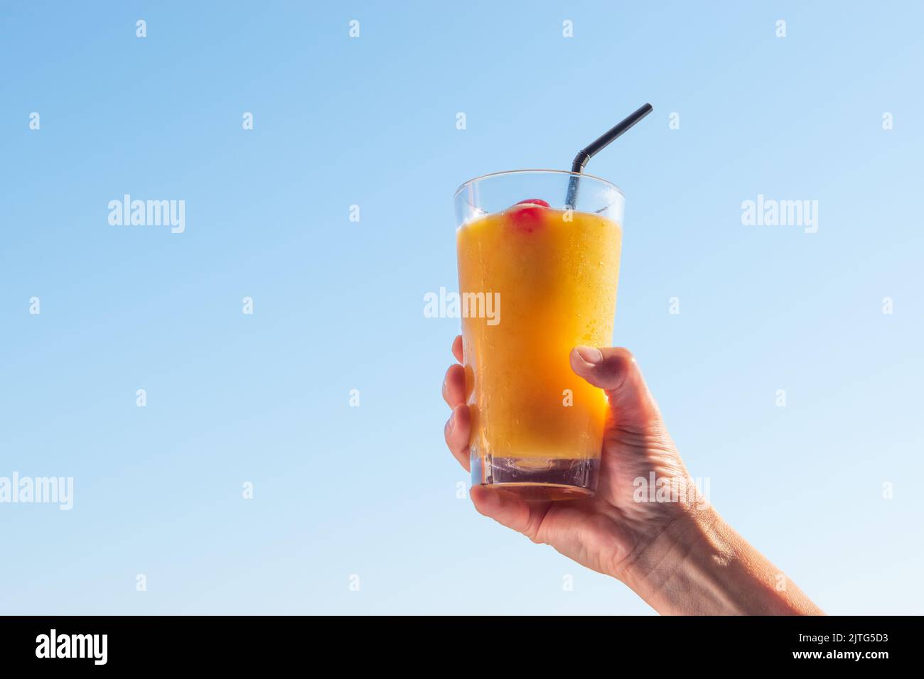 Bicchiere rialzato a mano da donna con cocktail d'arancia rinfrescante nell'aria. Foto Stock