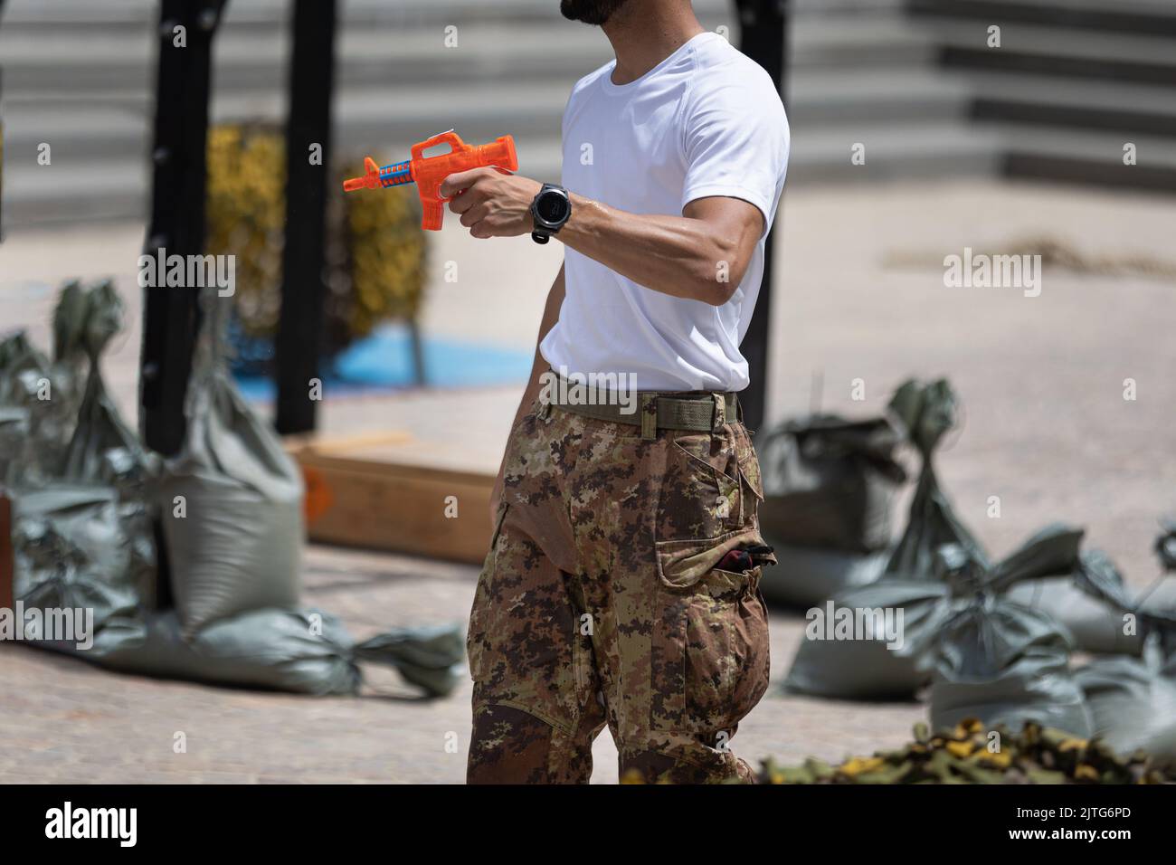 Soldato in uniforme e pantaloni Camouflage sparando giocosamente una pistola ad acqua arancione. Foto Stock