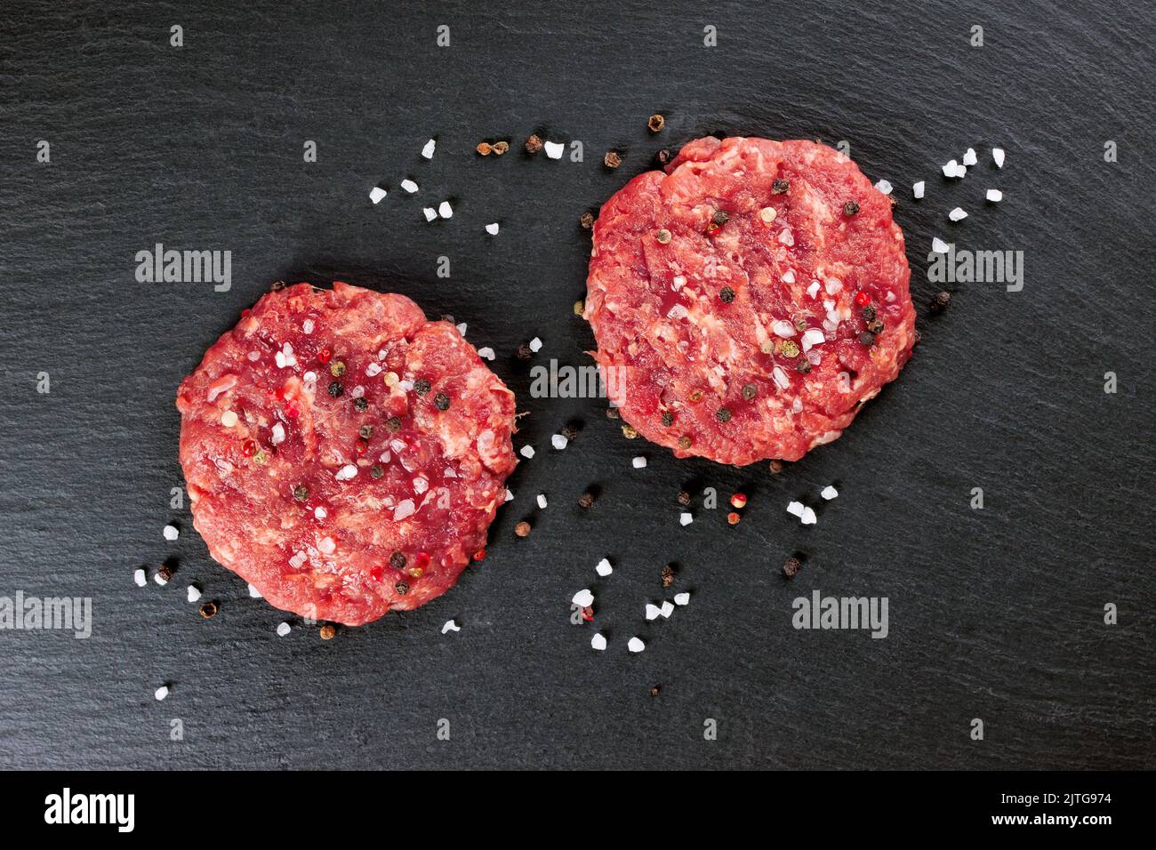 Hamburger di bistecca di manzo tritato fresco fatto in casa con spezie e cipolla, su un tavolo di ardesia nera, spazio copia, vista dall'alto Foto Stock