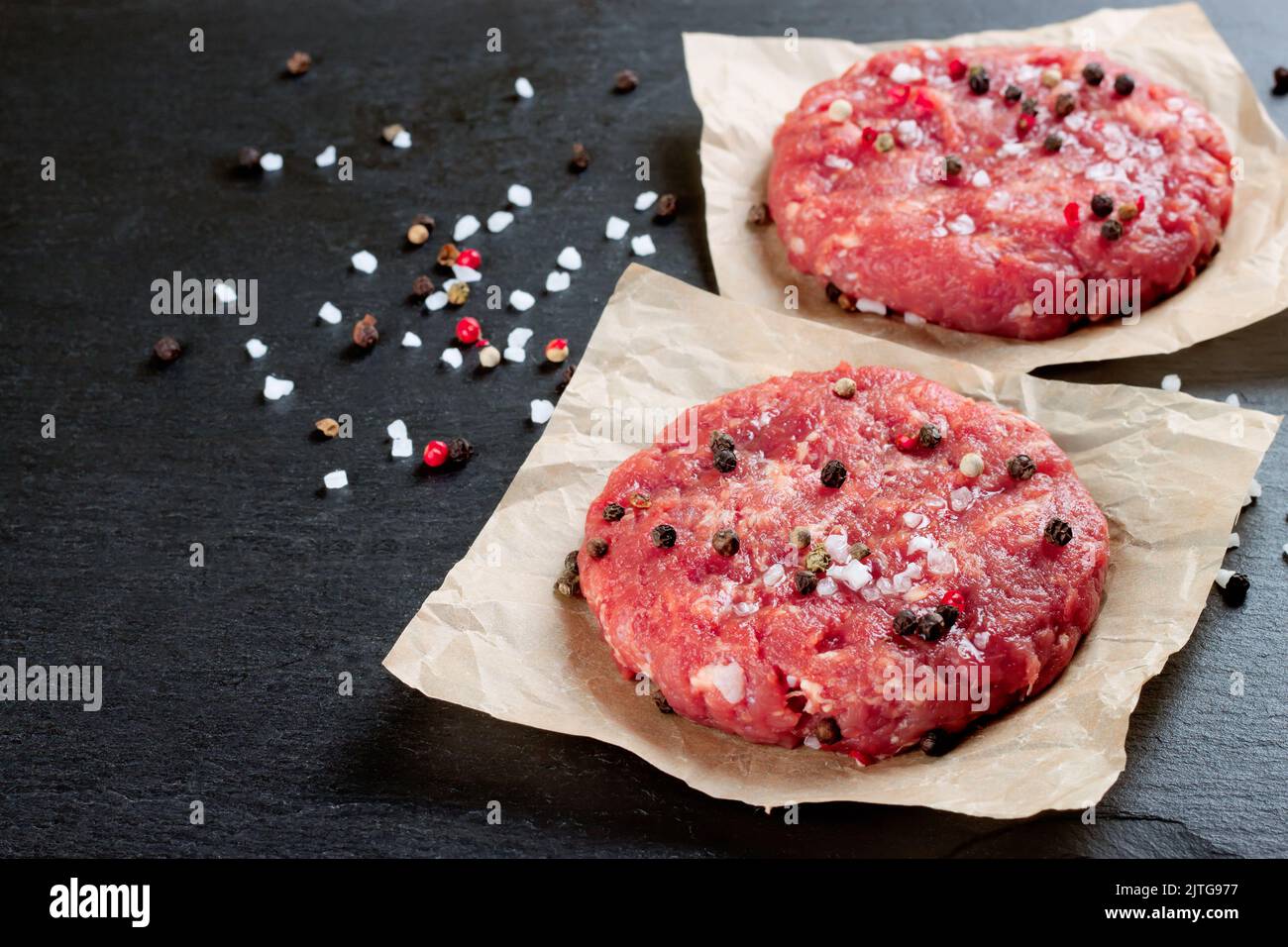 Hamburger di bistecca di manzo tritato fresco e crudo fatto in casa con spezie, su un tavolo nero ardesia, spazio copia Foto Stock