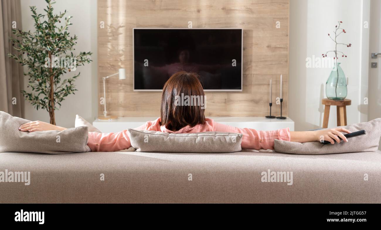 Ragazza in una posa di riflessione sul divano nel soggiorno di fronte alla TV Foto Stock
