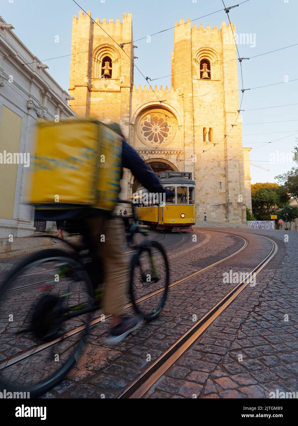 La Cattedrale di Santa Maria maggiore, nota anche come Cattedrale di Lisbona (sé de Lisboa). Tram e un ciclista di consegna con una borsa gialla davanti. Estate sera. Foto Stock