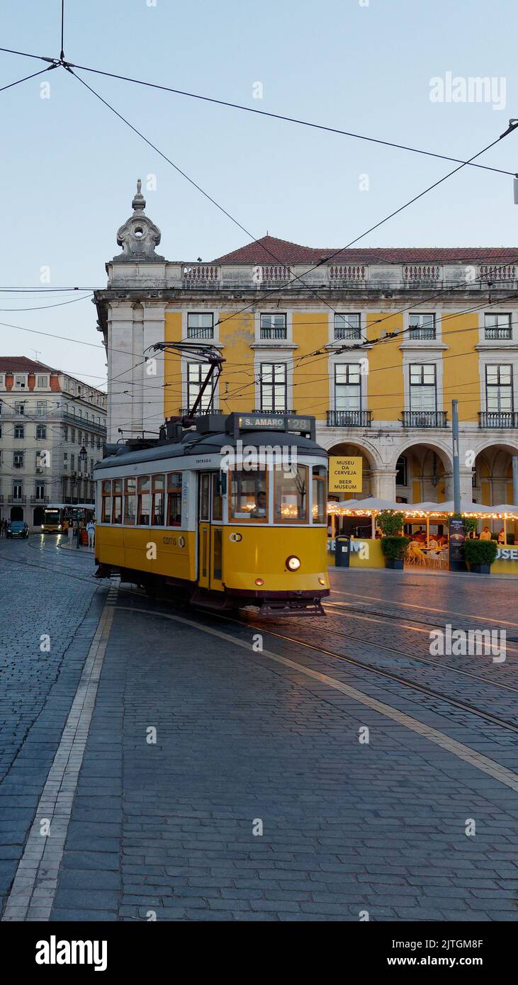 Praa do Comércio (Piazza del Commercio) a Lison in una serata estiva bagnata mentre un tram aka Streetcar aka Trolley passa davanti agli edifici gialli Foto Stock