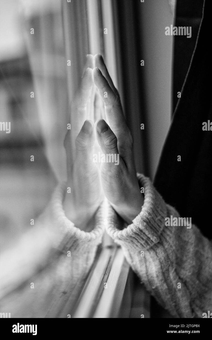 Immagine verticale di una mano sul vetro di una finestra in scala di grigi Foto Stock