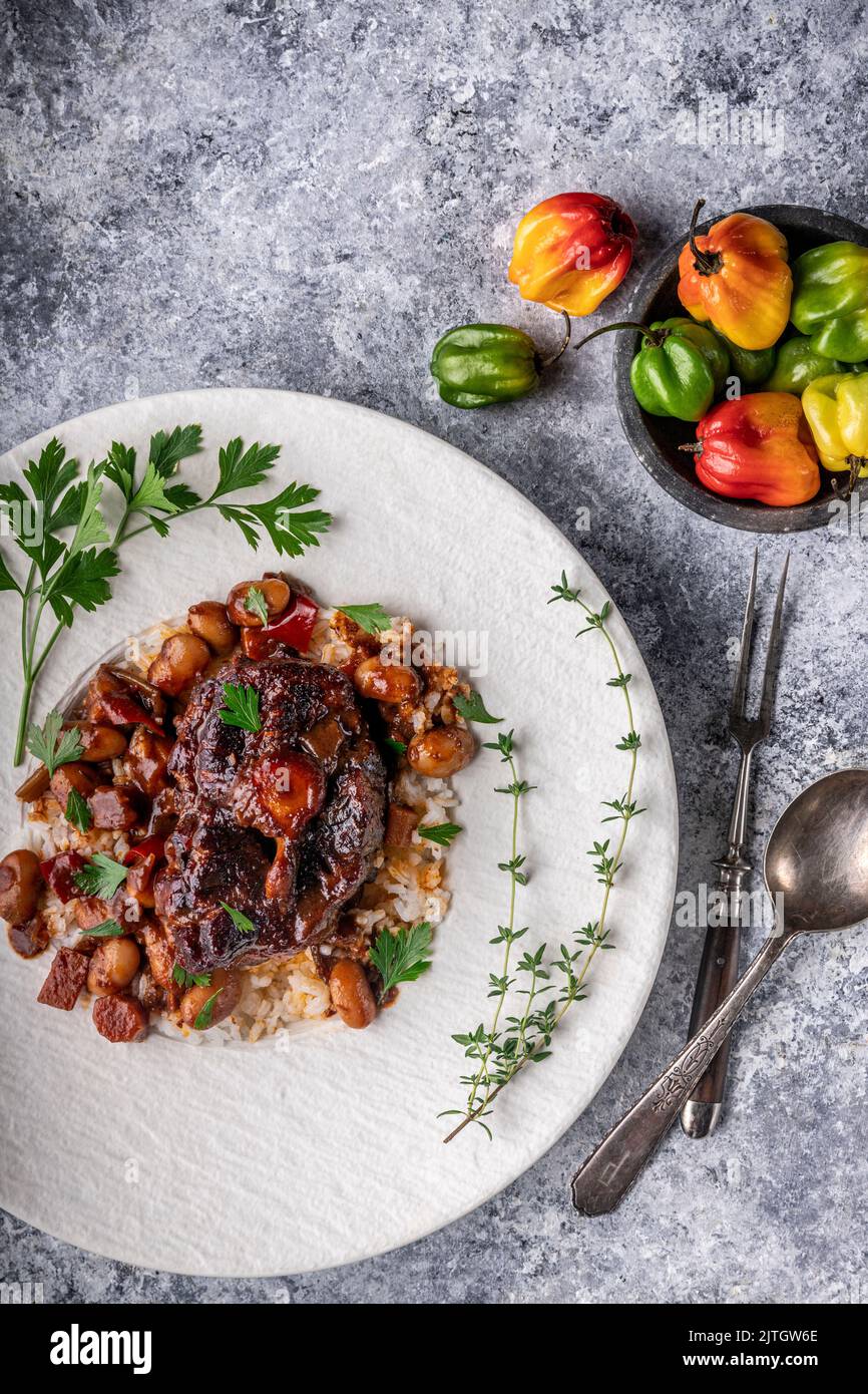 Coda di bue con osso, salsa e riso su piatto bianco con contorno alle erbe e peperoni in ciotola Foto Stock