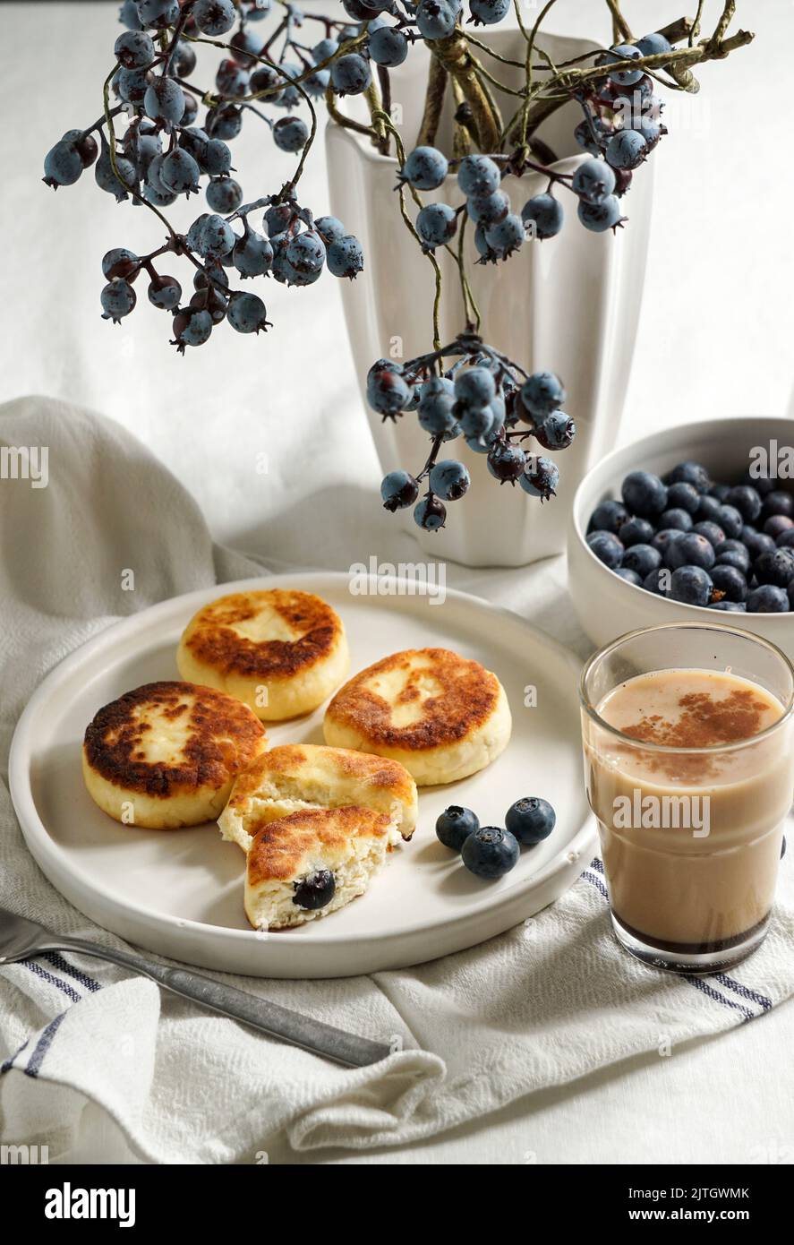 Syrniki con mirtilli e caffè. Colazione gustosa. Frittelle fritte di quark (formaggio cagliato); Foto Stock