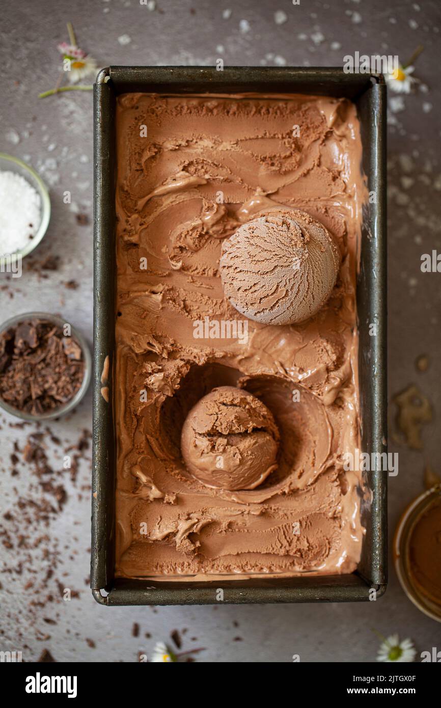 Gelato al cioccolato in una teglia di metallo con due palline e ingredienti che circondano la teglia. Foto Stock