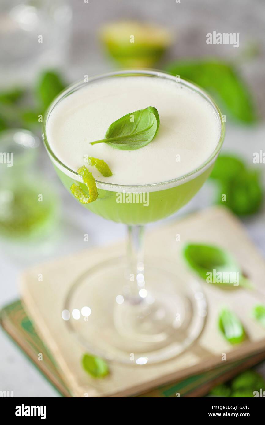 Un cocktail di gin al basilico con schiuma di albume e contorno fresco di basilico e scorza di lime. Foto Stock