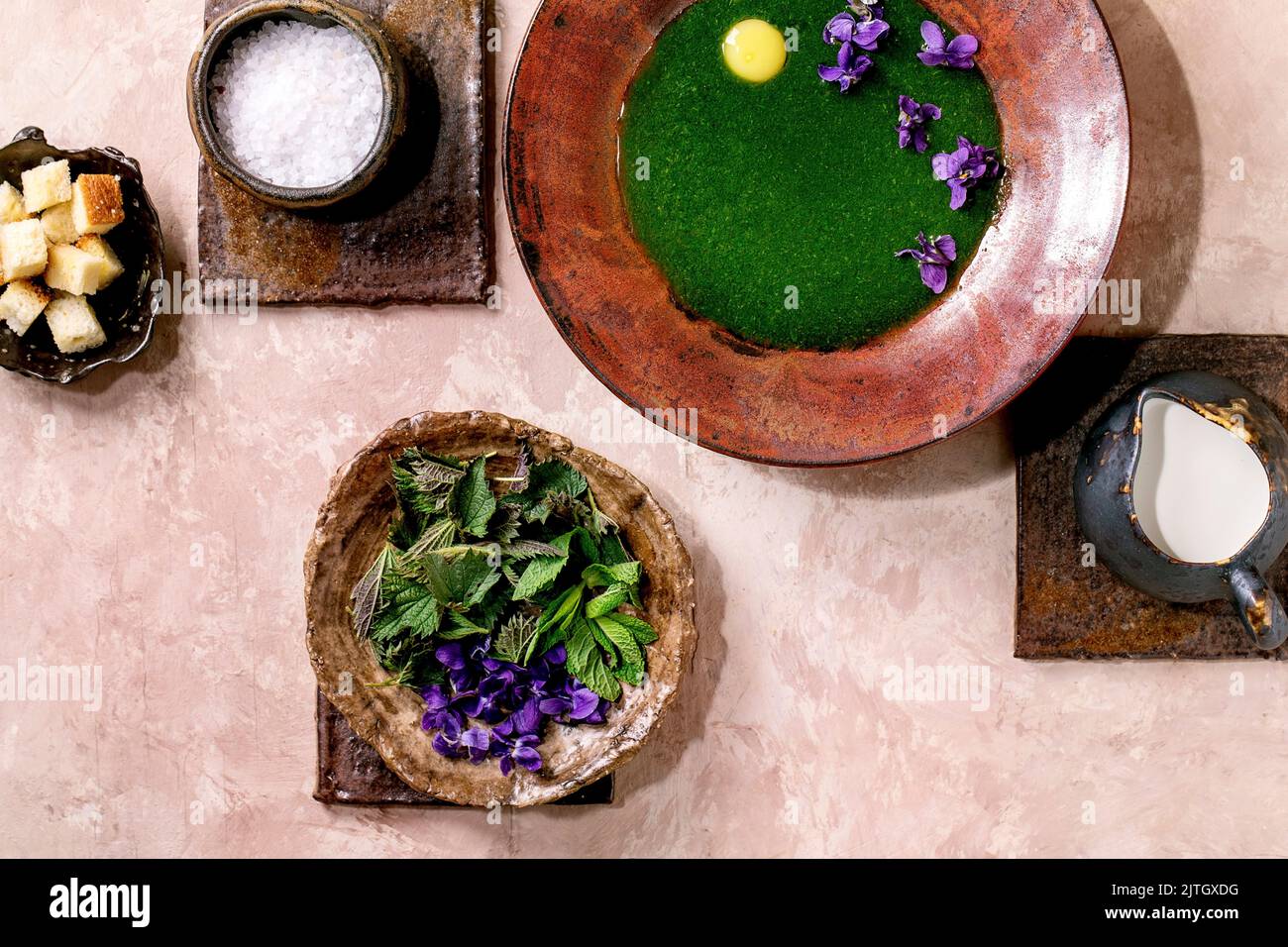 Piatto di zuppa di purea di ortica primaverile, servito con tuorlo di quaglia, fiori di violette, crema, crostini e giovani foglie di ortica su piastrelle di ceramica marrone. P Foto Stock