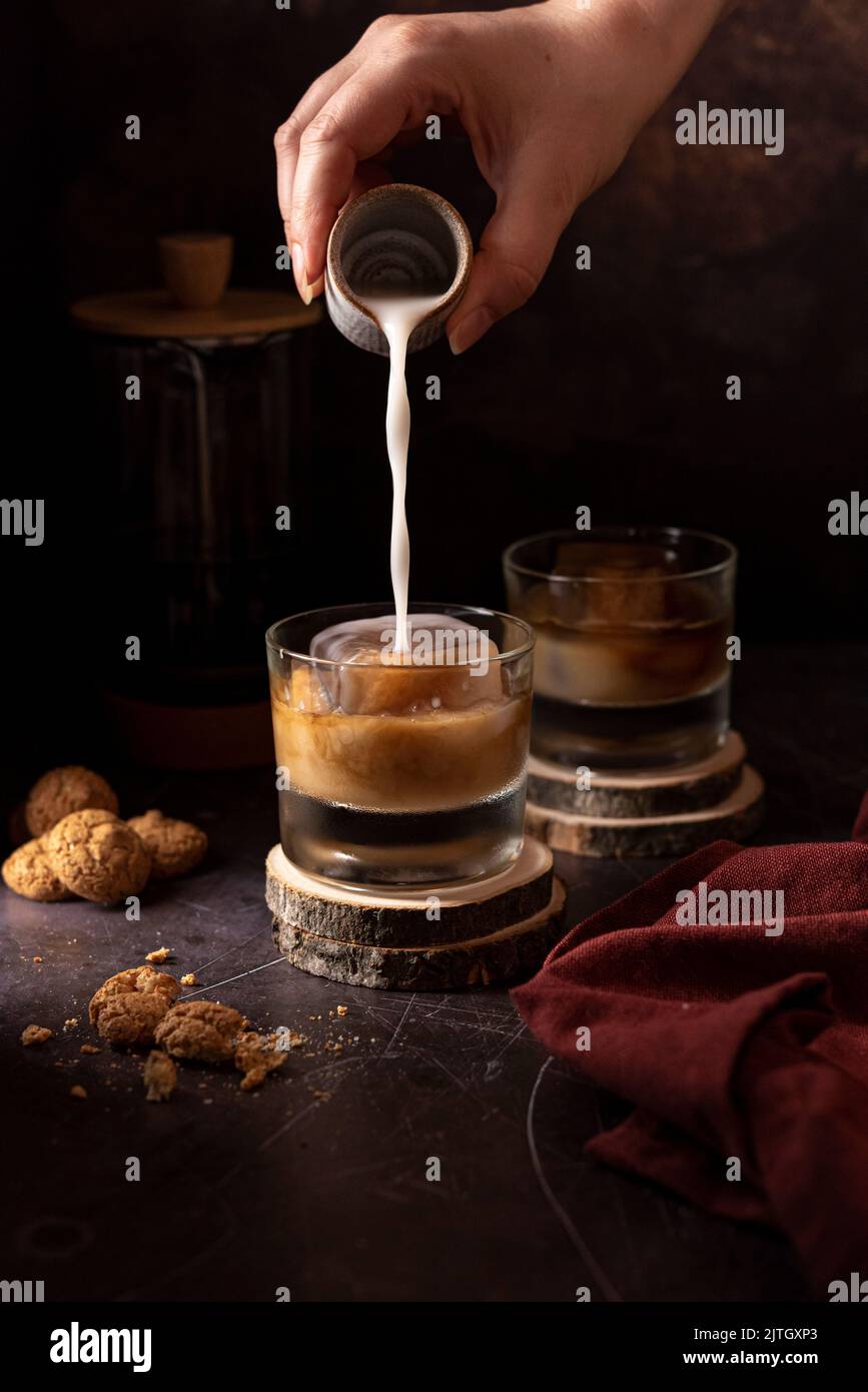 Versare il latte in un caffè ghiacciato su uno sfondo scuro Foto Stock
