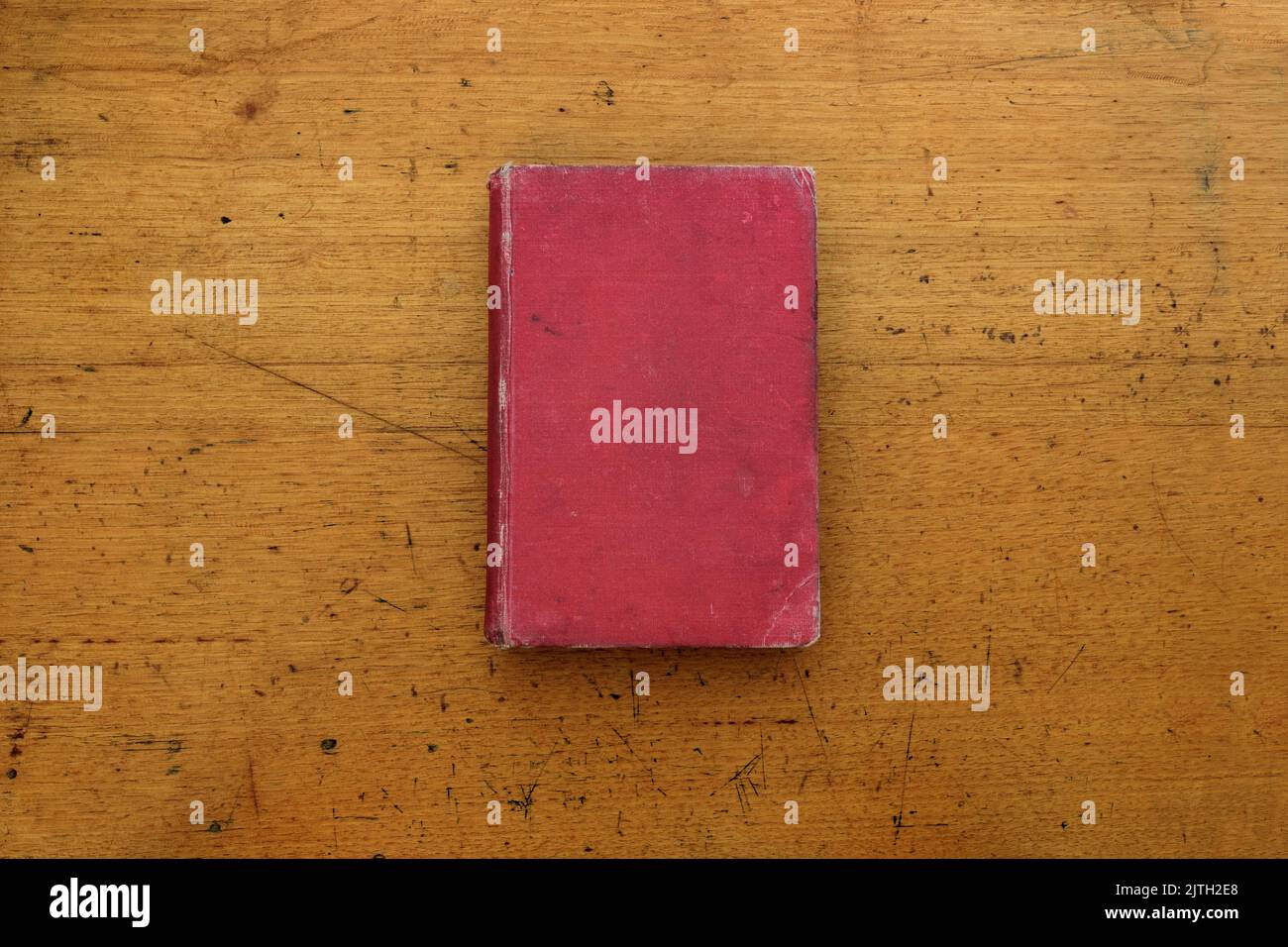 Un libro d'antiquariato con una copertina rigida in tessuto rosso che siede sopra un vecchio banco di scuola di legno, fotografato dall'alto. Foto Stock