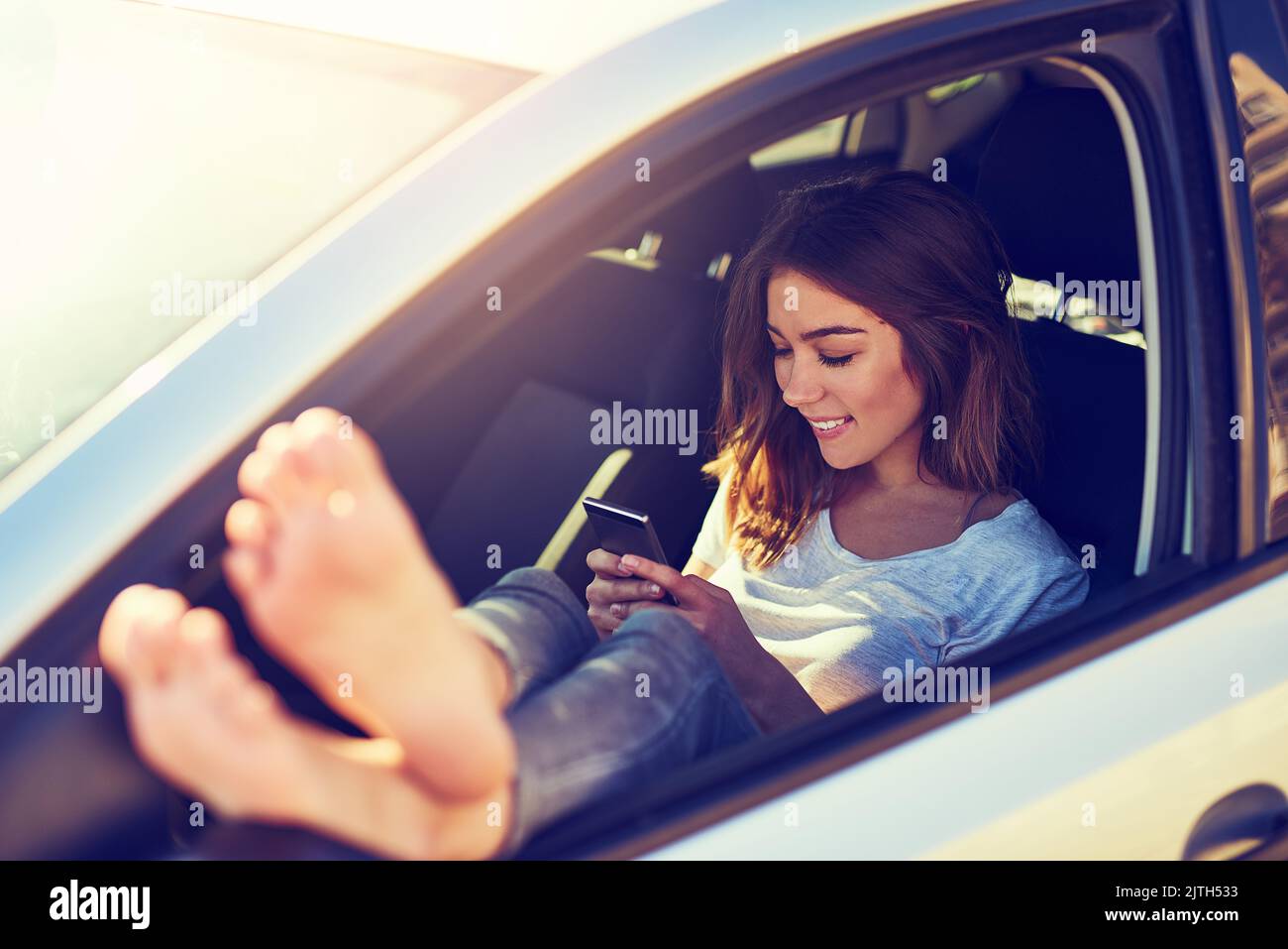 Invio di un testo dalla strada. Una giovane donna che invia un messaggio di testo mentre si siede in auto. Foto Stock