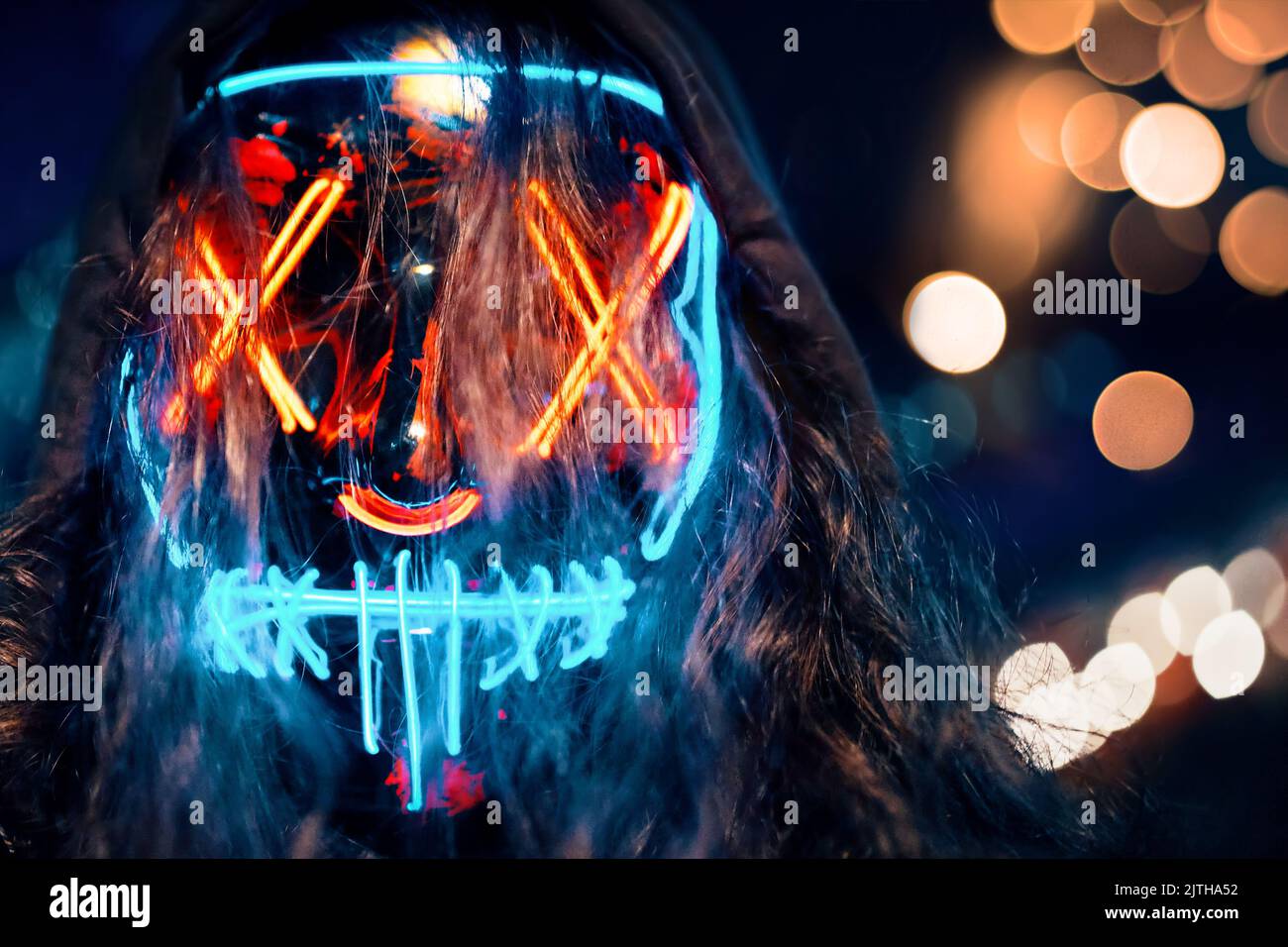 Uomo con felpa con cappuccio e capelli lunghi dispettati in una maschera luminosa al neon. Foto Stock