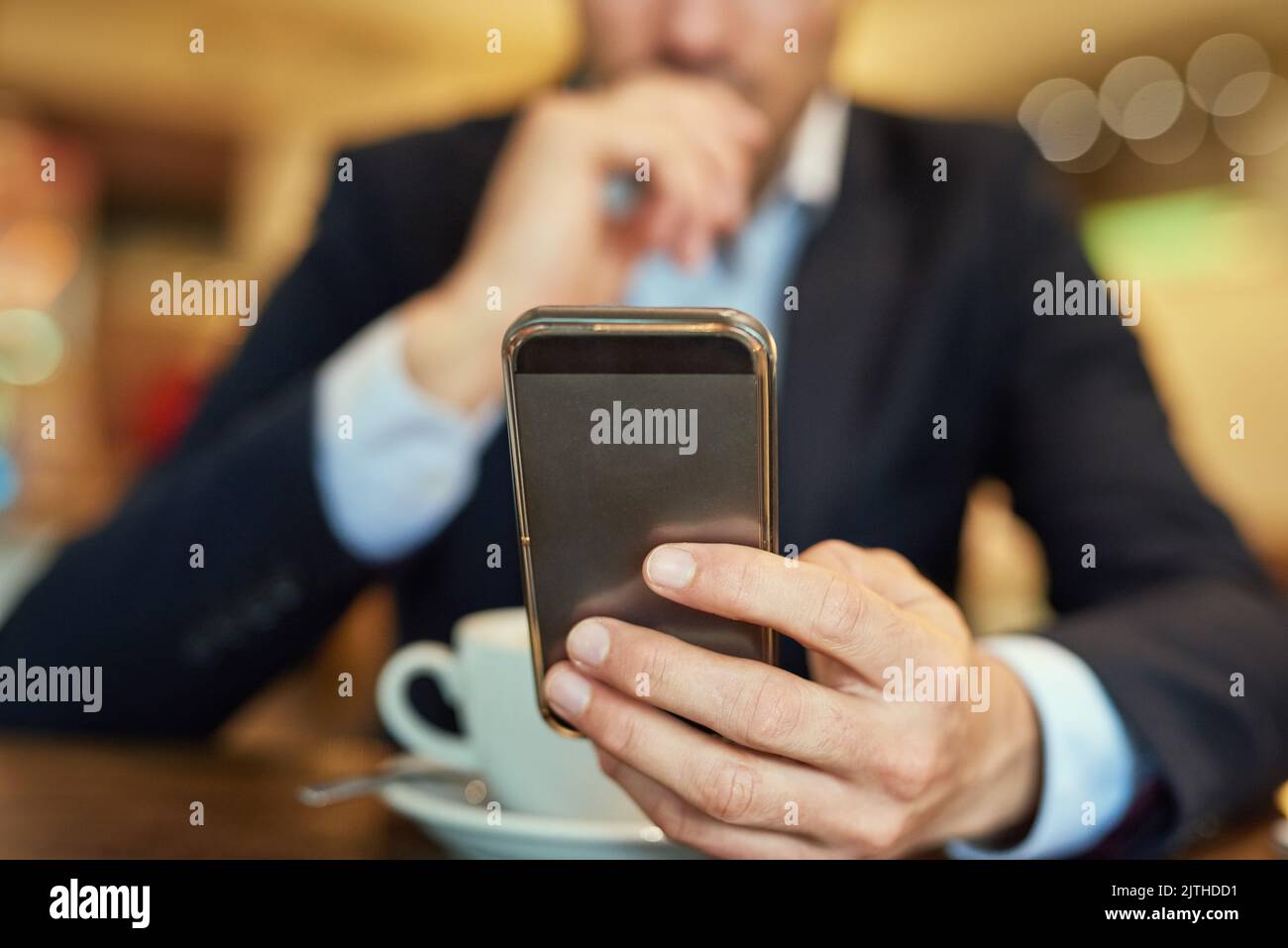 Cosa c'è di nuovo all'ordine del giorno: Un uomo d'affari irriconoscibile che invia un messaggio di testo mentre si siede in una caffetteria. Foto Stock