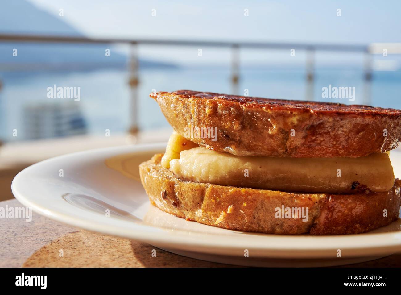 Colazione dolce con toast alla griglia, banana e cannella sulla terrazza di un hotel sul mare. Vacanze estive e viaggi Foto Stock