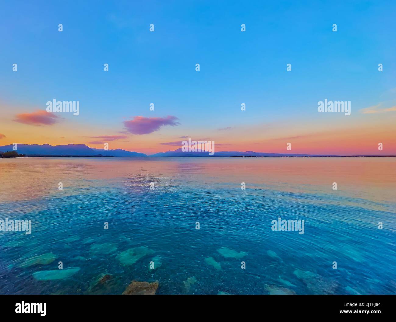 Il pittoresco tramonto sul Lago di Garda con la sua superficie ondulata e le sagome delle Prealpi del Garda sullo sfondo, Desenzano del Garda Foto Stock
