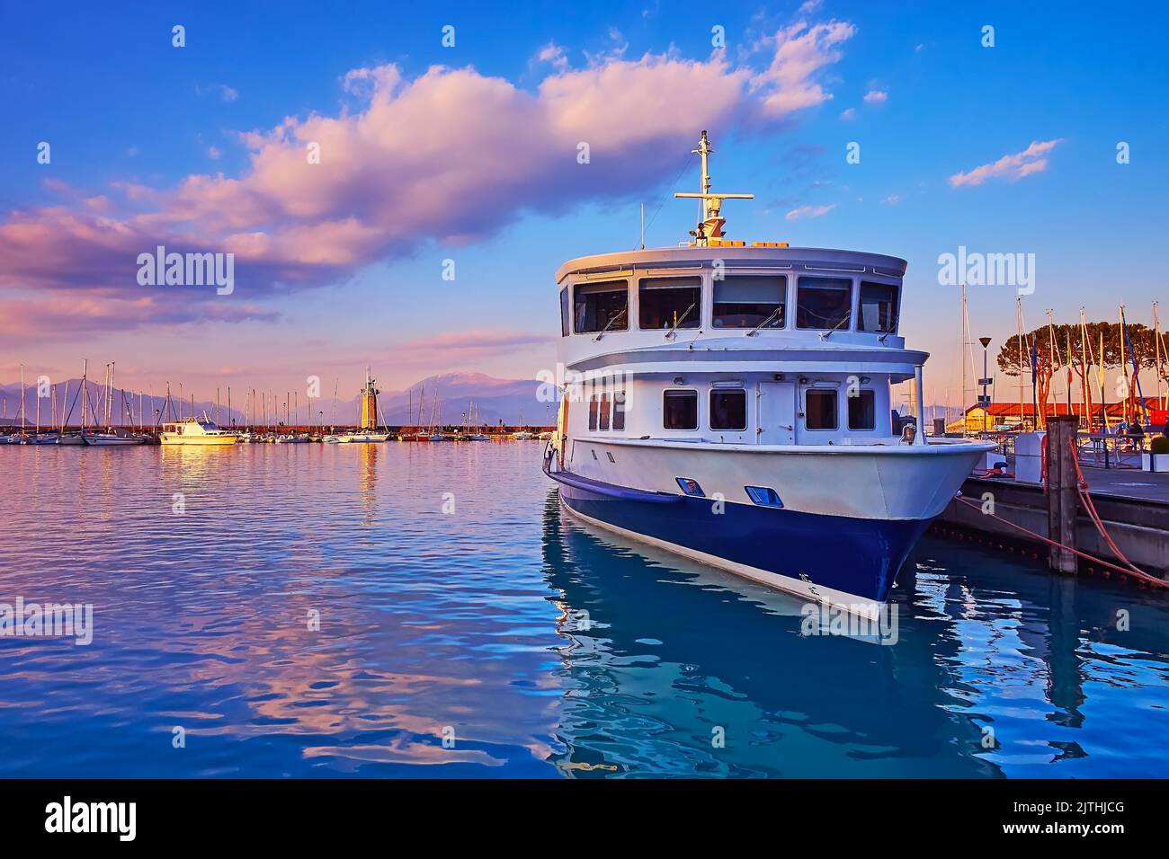 Il tramonto viola sul Lago di Garda con traghetto ormeggiato, yacht in porto e faro di Faro in pietra, Desenzano del Garda, Italia Foto Stock