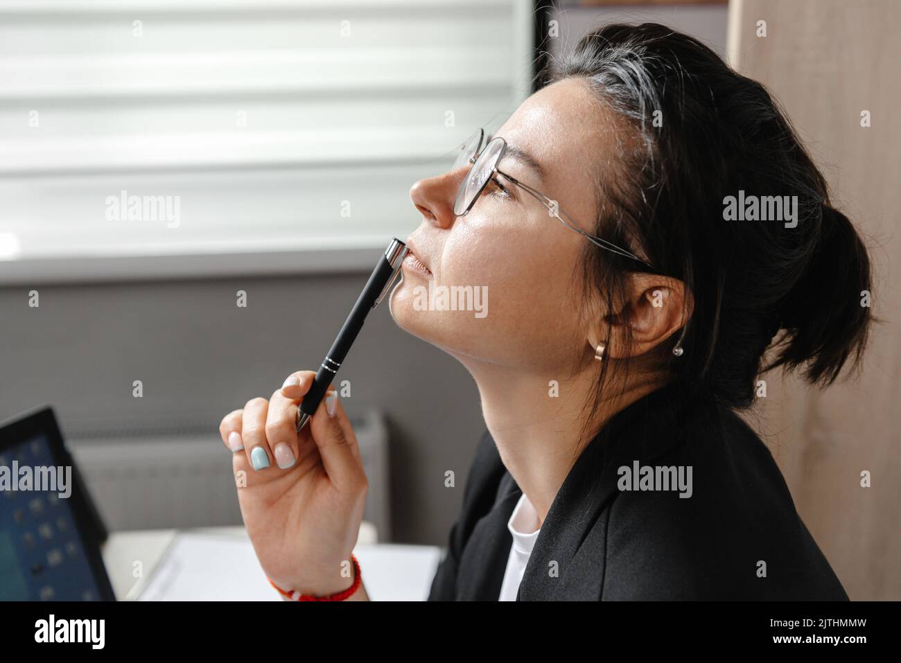 Giovane donna attraente alla scrivania in ufficio, che lavora con il notebook, accanto alla finestra, pensando alla posta, blogger a tempo pieno, alla ricerca di ispirazione Foto Stock