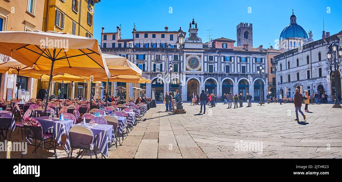 BRESCIA, ITALIA - 10 APRILE 2022: I ristoranti all'aperto con riccamente decorata Torre dell'Orologio con orologio astronomico, situati sulla P Foto Stock