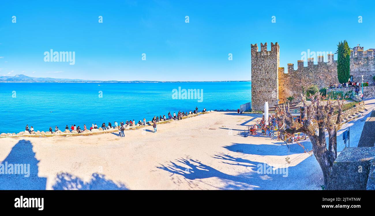 SIRMIONE, ITALIA - 10 APRILE 2022: Castello Scaligero sulla riva del Lago di Garda con spiaggia e Prealpi del Garda sullo sfondo, il 10 aprile a Sirmione Foto Stock