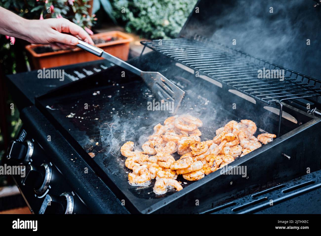 Grigliare i gamberetti sullo spiedino alla griglia all'aperto. Gamberetti grigliati sulla griglia fiammeggiante. Uomo a mano con tenaglia pizzicando pesce alla griglia Foto Stock