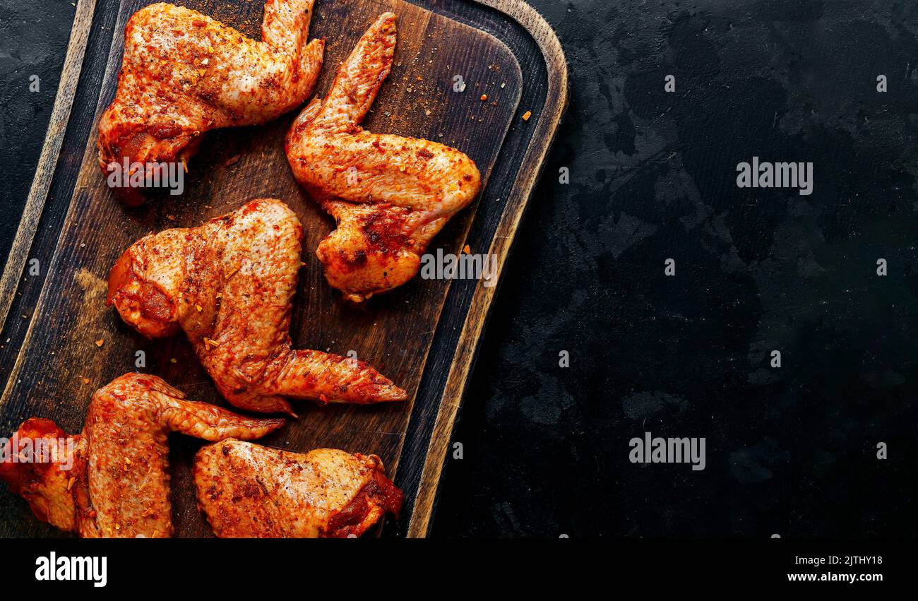 Ali di pollo crude marinate in paprika e curry. Spazio di copia. Carne cruda su un tagliere. Sfondo scuro, vista dall'alto. Foto Stock