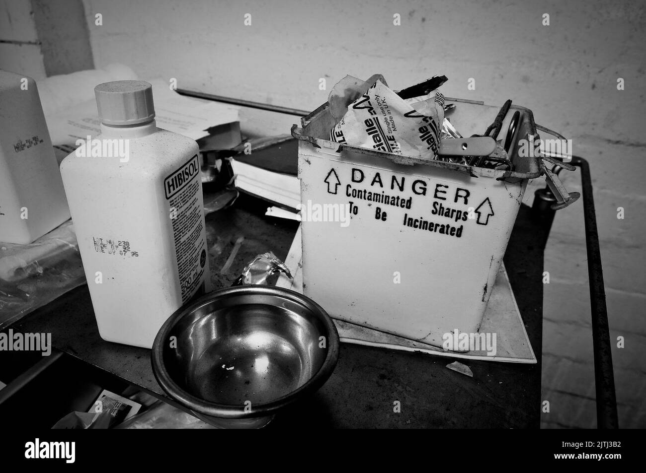 Scatola di oggetti taglienti piena di oggetti appuntiti come aghi e lame chirurgiche su un carrello in un mortuario abbandonato. Foto Stock