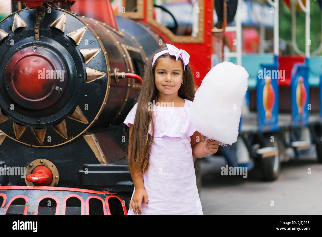 La bambina in un parco divertimenti d'estate mangia caramelle di cotone e sorride felicemente. Il concetto di vacanze estive e vacanze scolastiche Foto Stock