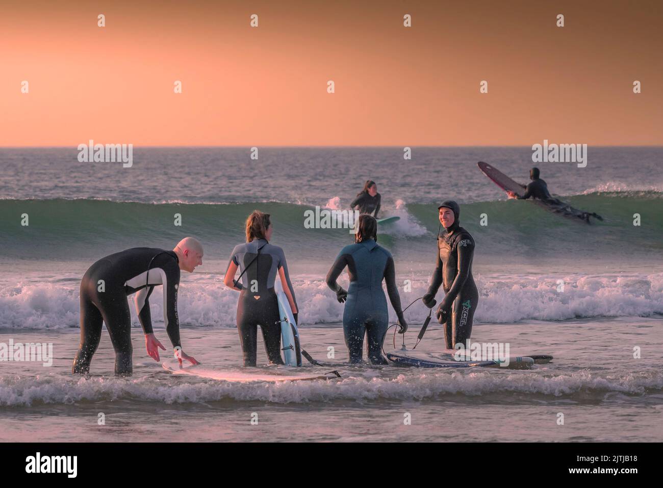 I surfisti possono godersi una sessione serale di surf mentre il sole tramonta su Fistral Beach alla fine della giornata più calda dell'anno a Newquay in Cornovaglia nel Foto Stock