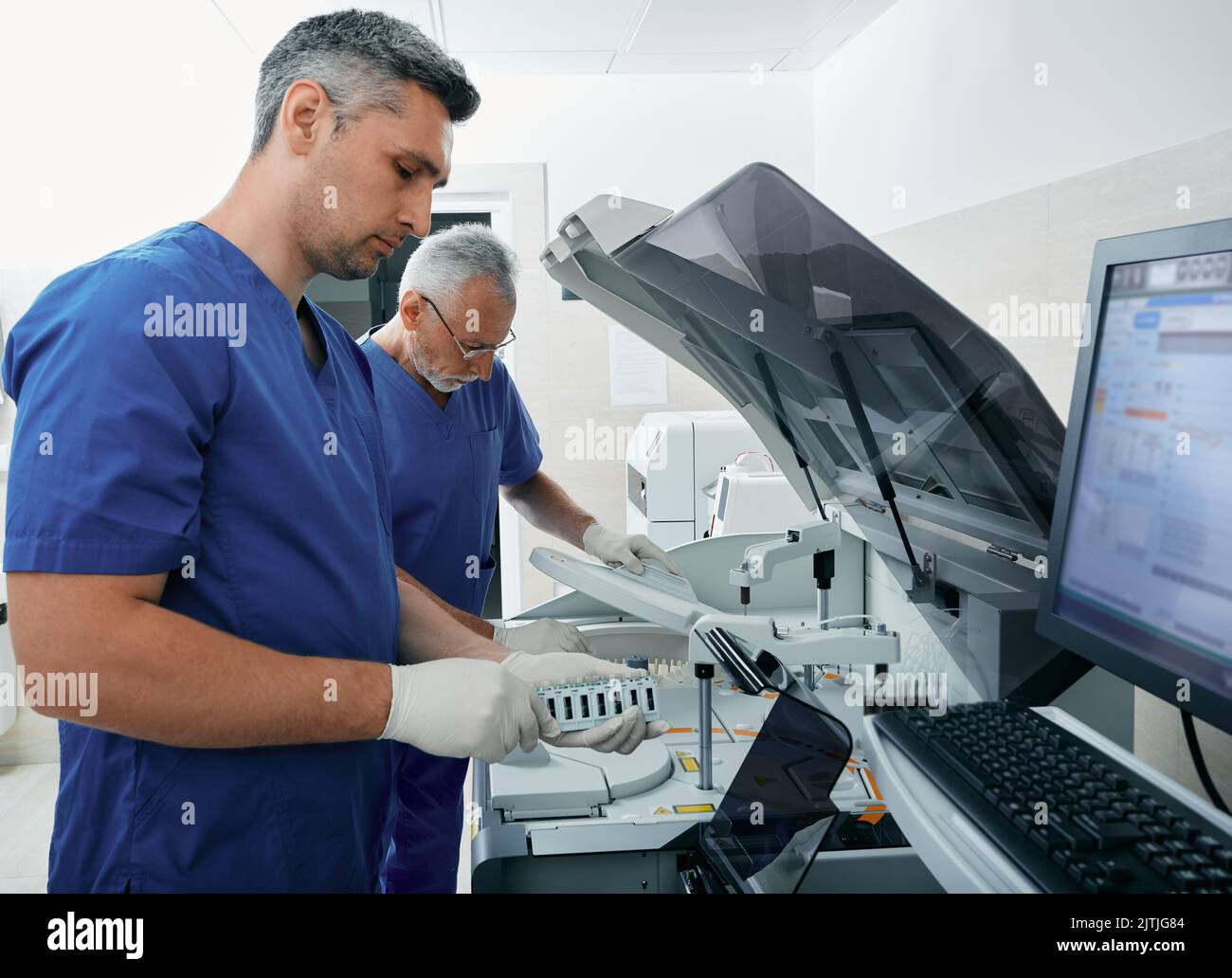 Assistenti di laboratorio che caricano i campioni di sangue nell'analizzatore automatico biochimico del sangue. Moderno laboratorio di ricerca medica e tecnici di laboratorio Foto Stock