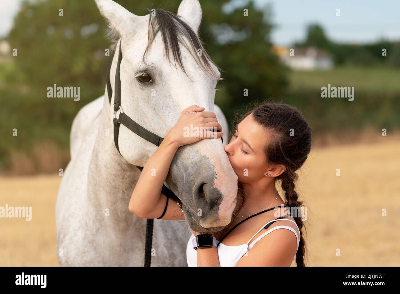 Bella giovane ragazza baciare la museruola di un cavallo bianco in un campo di fattoria in estate Foto Stock