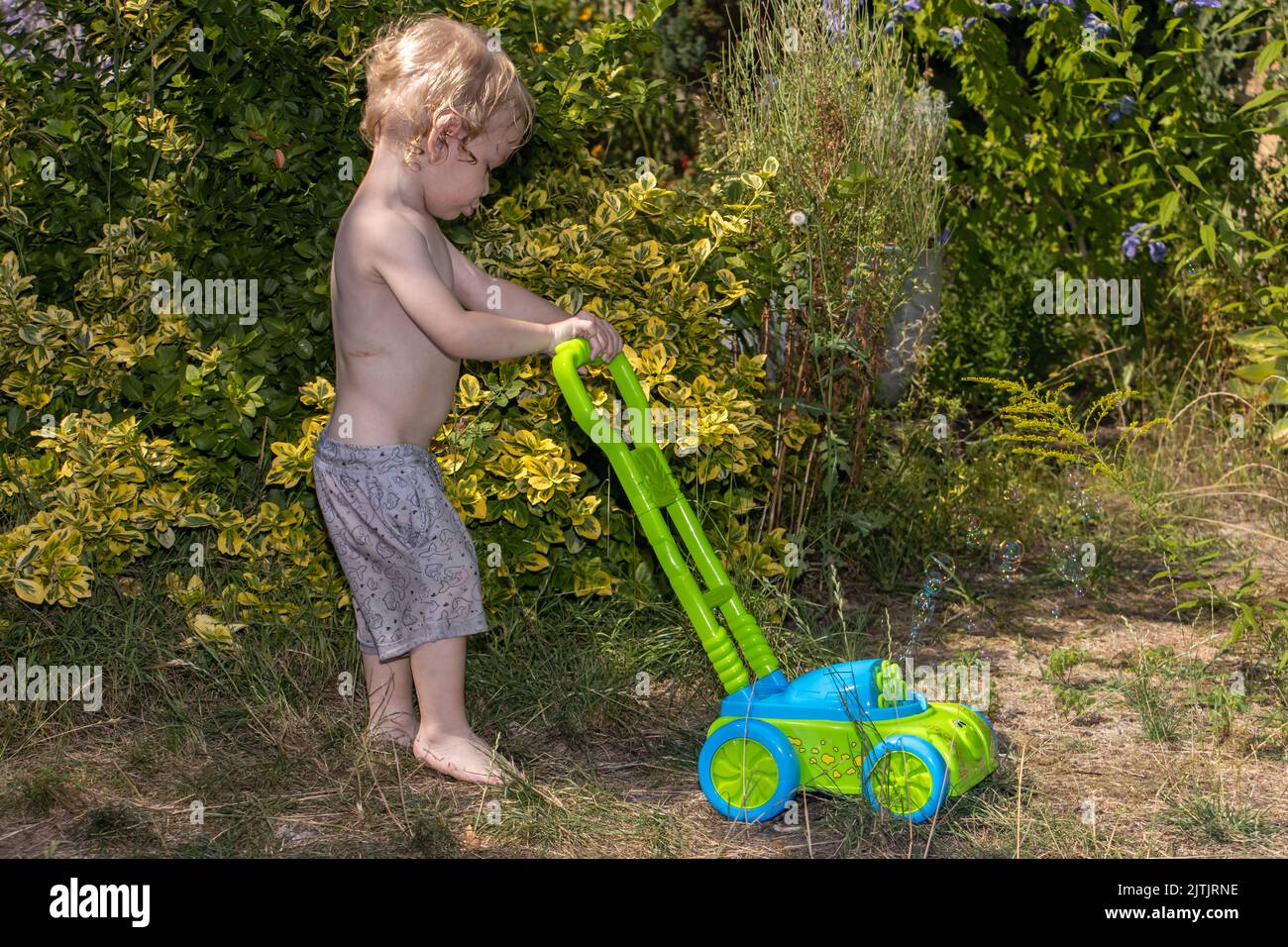 Un ragazzino spinge un tosaerba soffiando delle bolle nel giardino Foto Stock