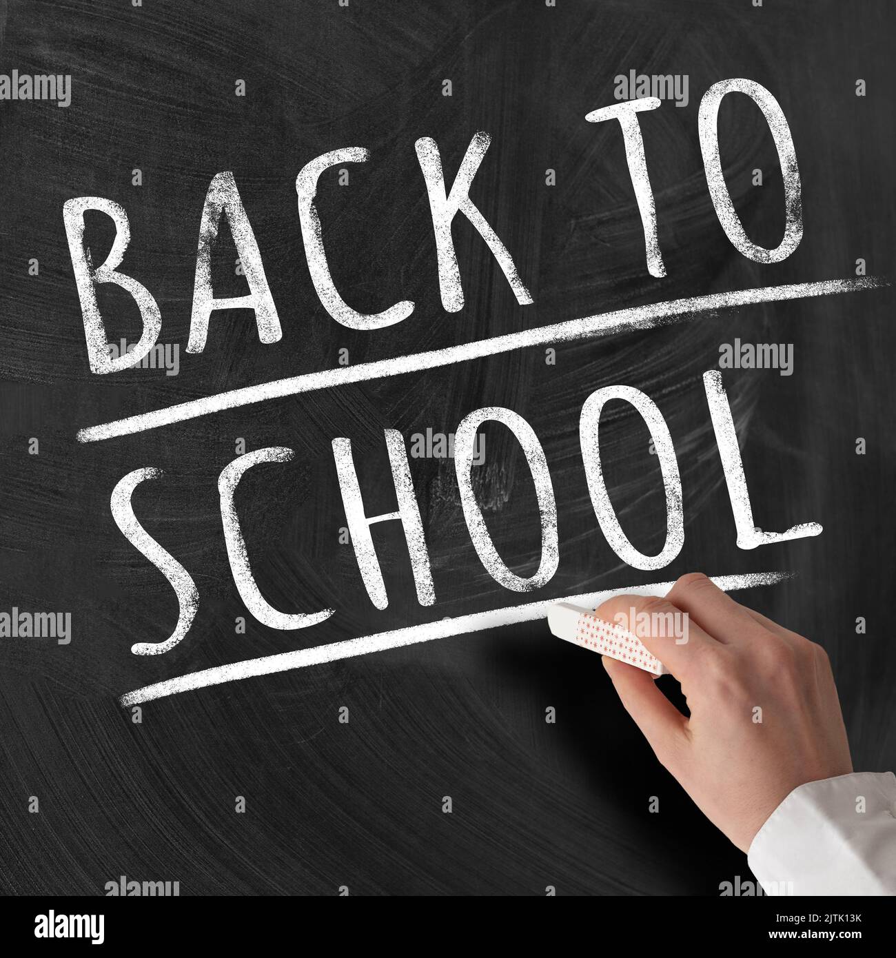 Mano dell'insegnante che tiene un pezzo di gesso contro la lavagna con testo DI RITORNO A SCUOLA Foto Stock