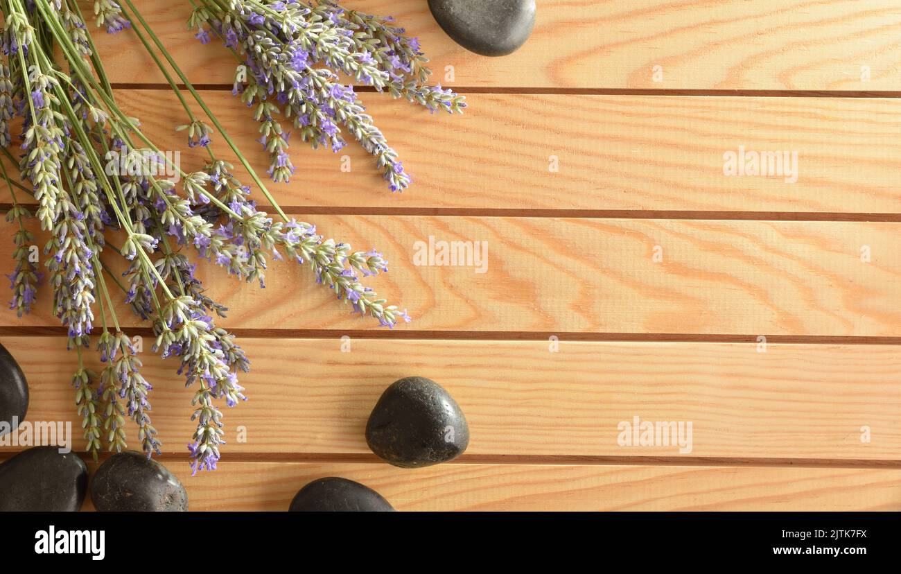 Concetto di benessere con stonesand nero e punte di lavanda fiorita su tavolo di legno. Vista dall'alto. Foto Stock