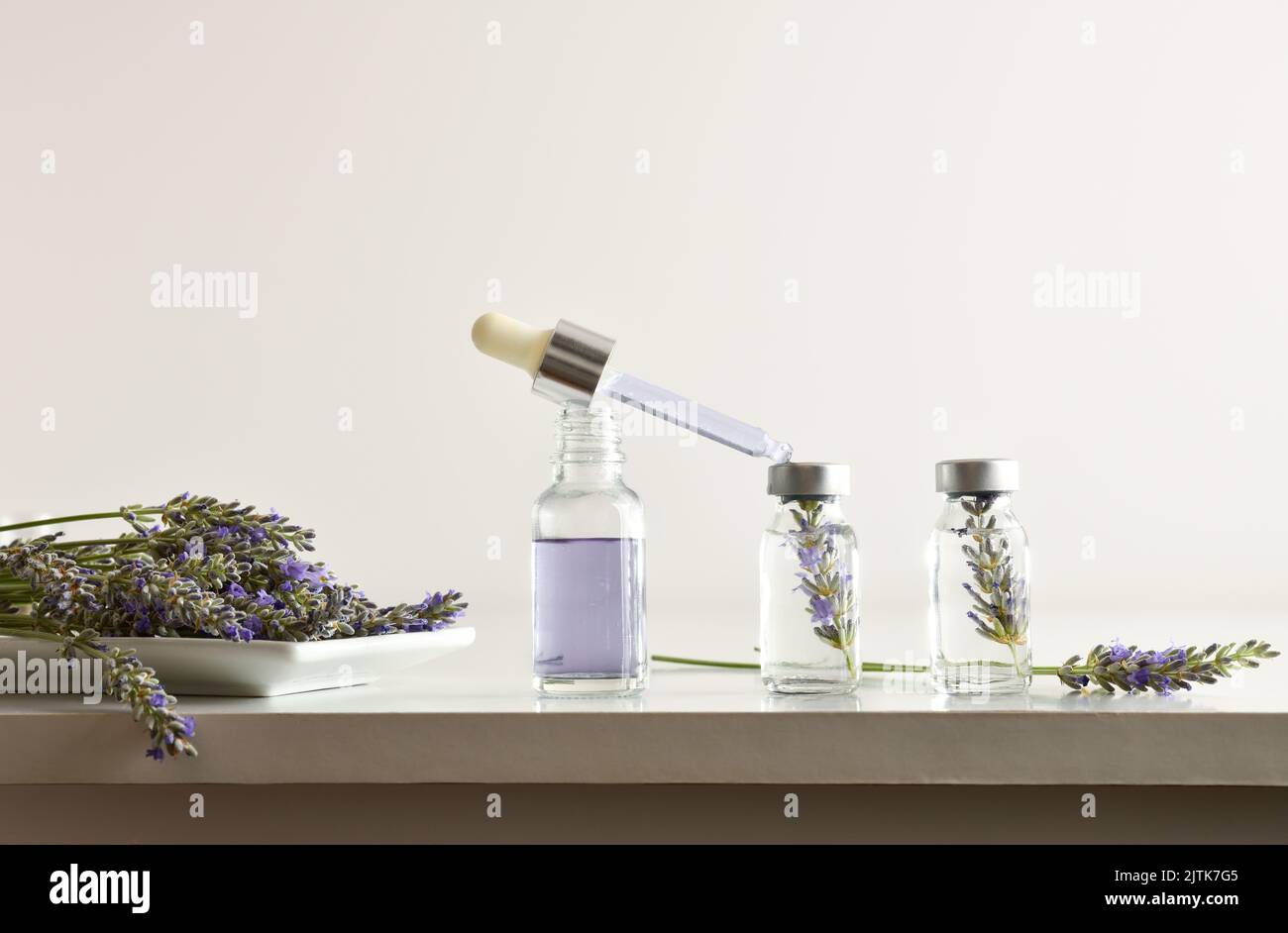 Fiale con preparazione di essenza di lavanda su un banco da laboratorio bianco e fondo isolato bianco. Vista frontale. Composizione orizzontale. Foto Stock
