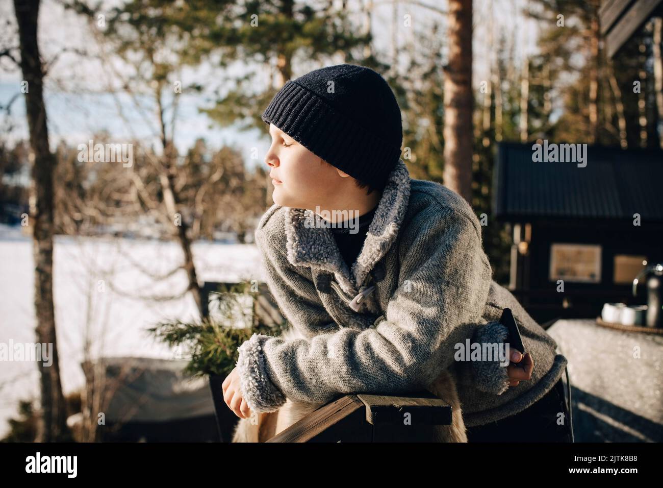 Ragazzo con gli occhi chiusi godendosi la luce del sole durante l'inverno Foto Stock